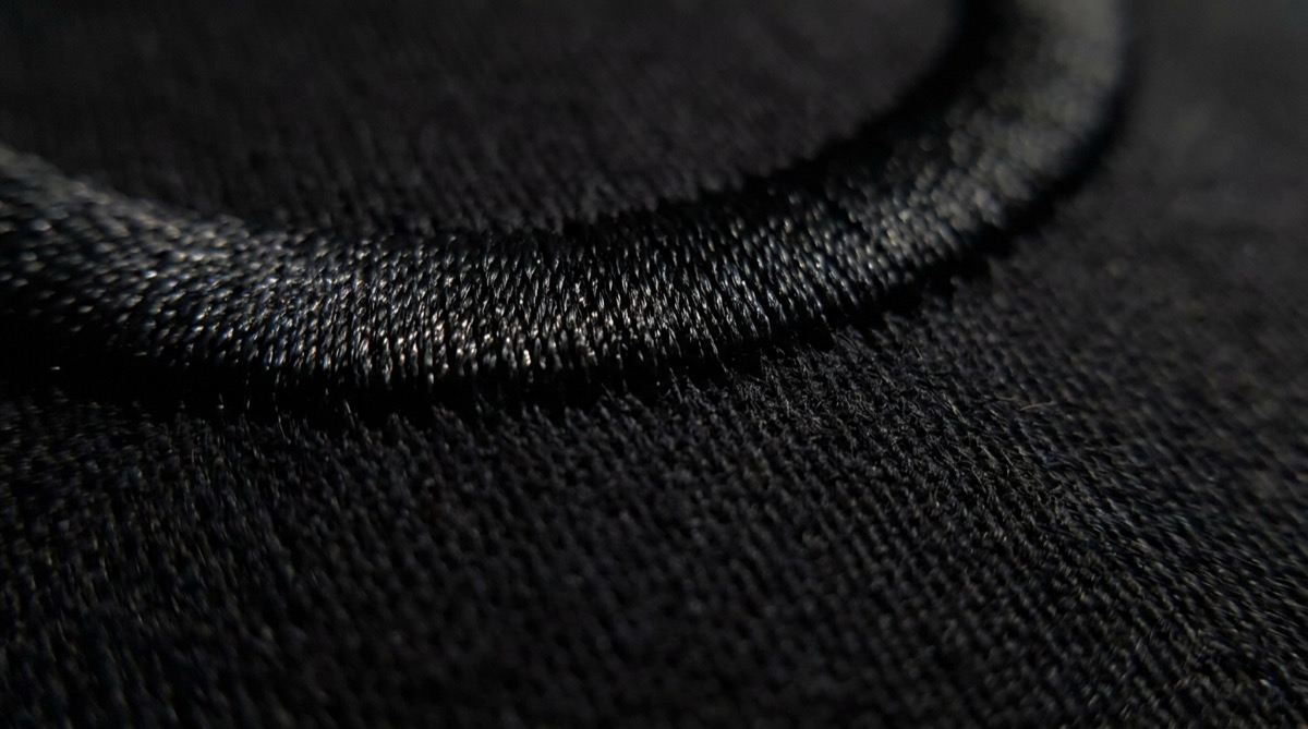 Macro photograph of black tonal satin stitch on black cotton, barely visible